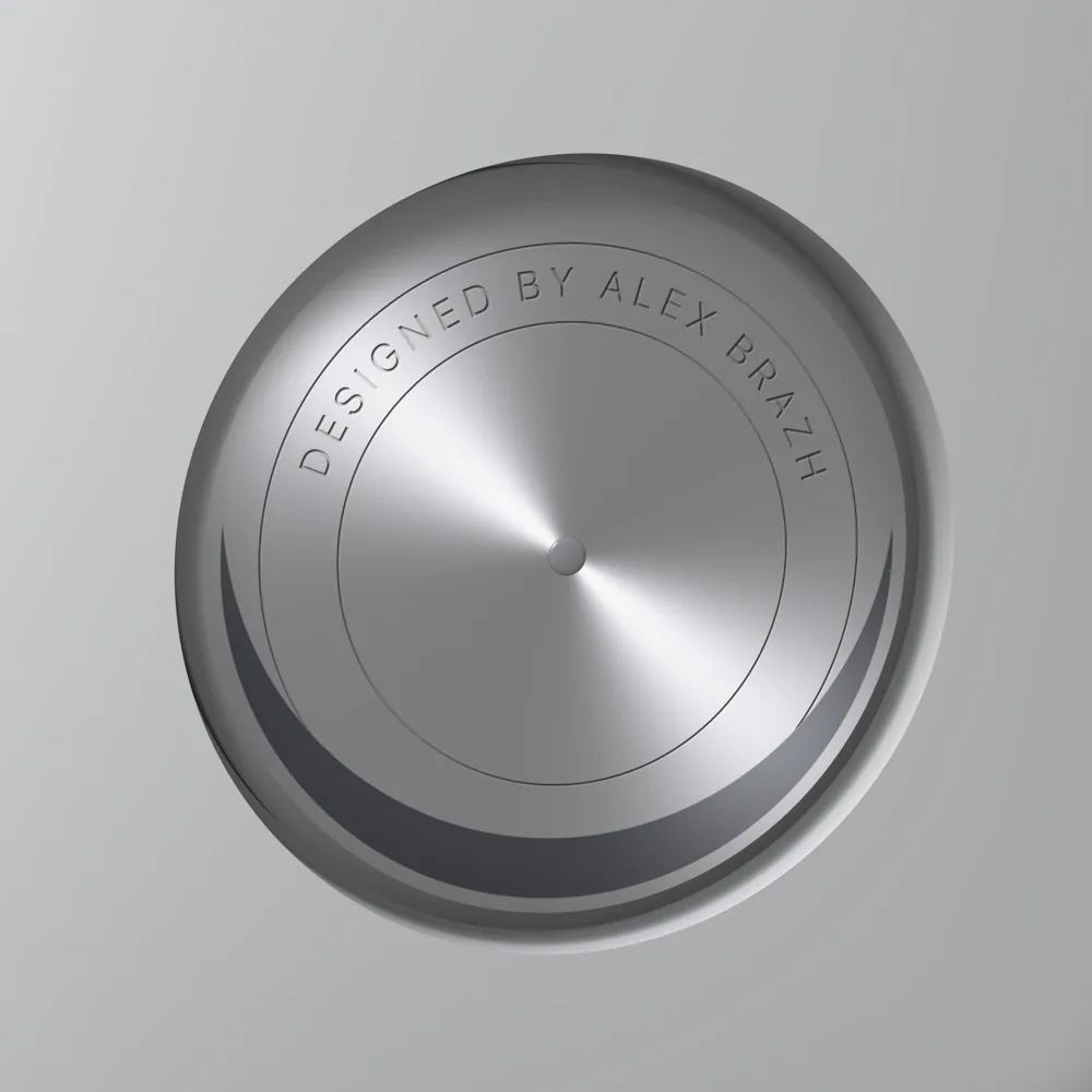 A close-up of the disk: brushed aluminium with a polished rivet at its centre, a dark steel crescent along its lower edge, and the words DESIGNED BY ALEX BRAZH engraved in spaced capitals round the top between two hairline circles
